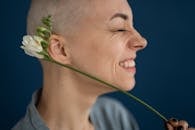 Side view of crop cheerful female patient with blossoming flower representing scar on head concept after brain tumor surgery on blue background