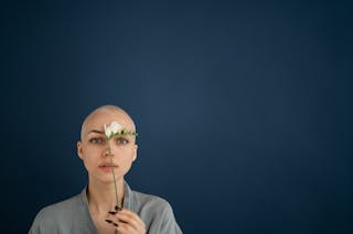 Young reflective female patient looking at camera with blooming flower representing cicatrice on forehead concept after cancer operation