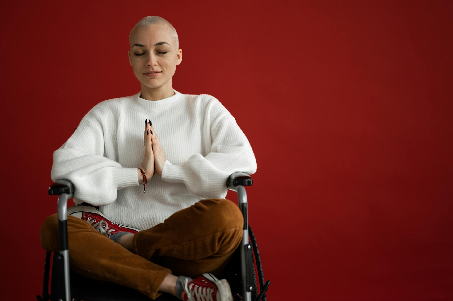 Young concentrated female with praying hands and crossed legs meditating during cancer recovery process on red background