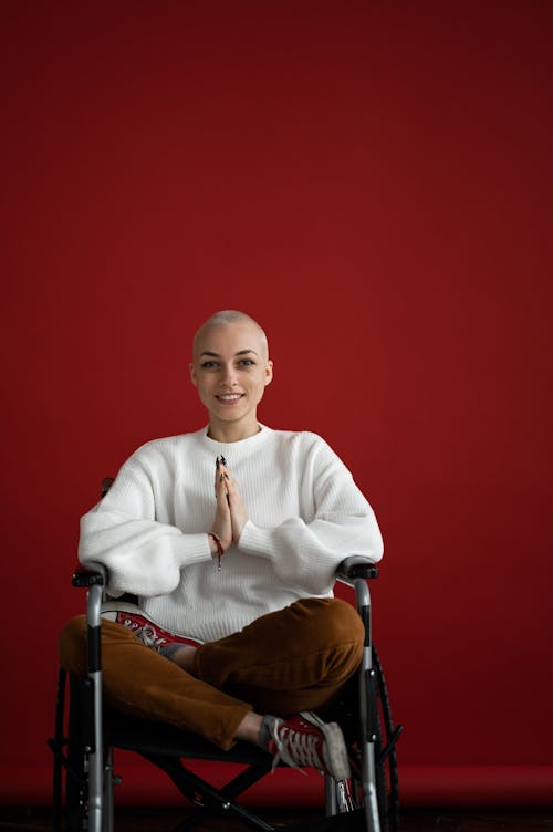 Free Young smiling female sitting in Lotus pose while looking at camera during cancer rehabilitation process on red background Stock Photo