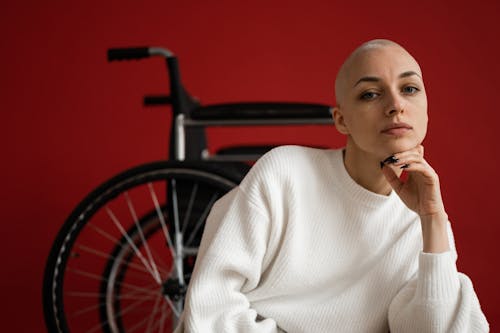 Free Woman with shaved head against wheelchair on red background Stock Photo