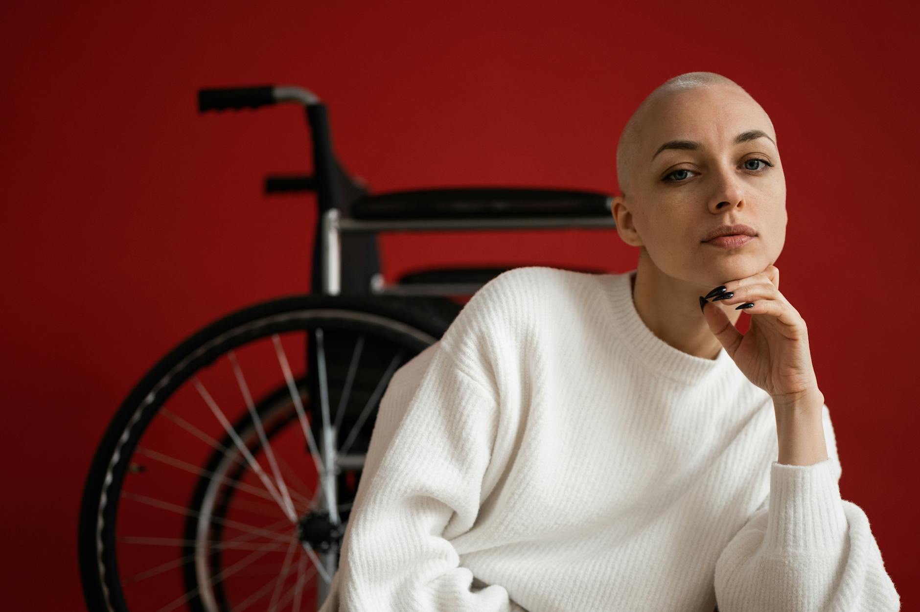 How to Set Realistic Financial Goals and Achieve Them Effortlessly 4 Portrait of a confident woman in white sweater sitting near a wheelchair against red background.