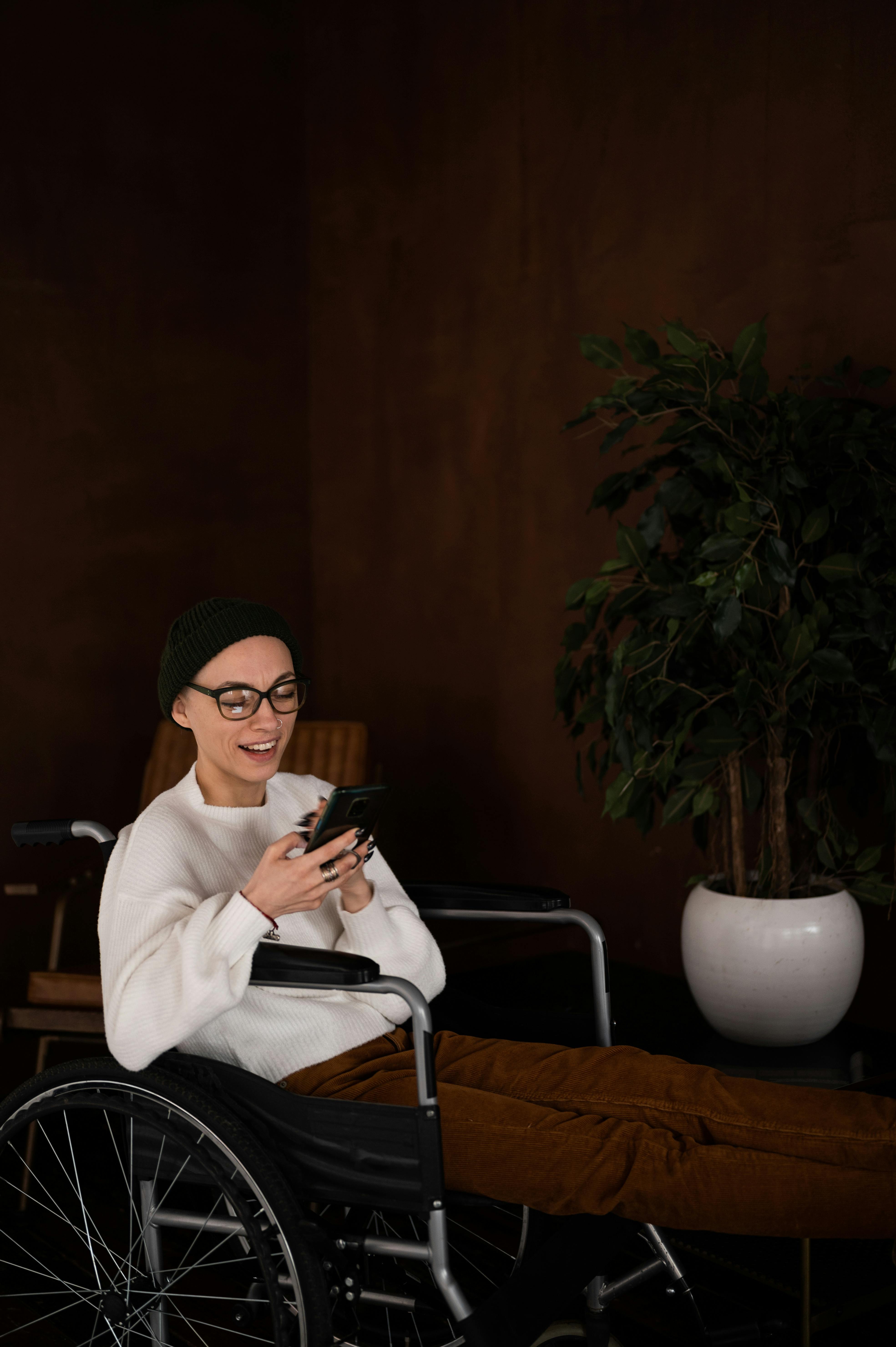 happy young woman sitting in wheelchair and using smartphone