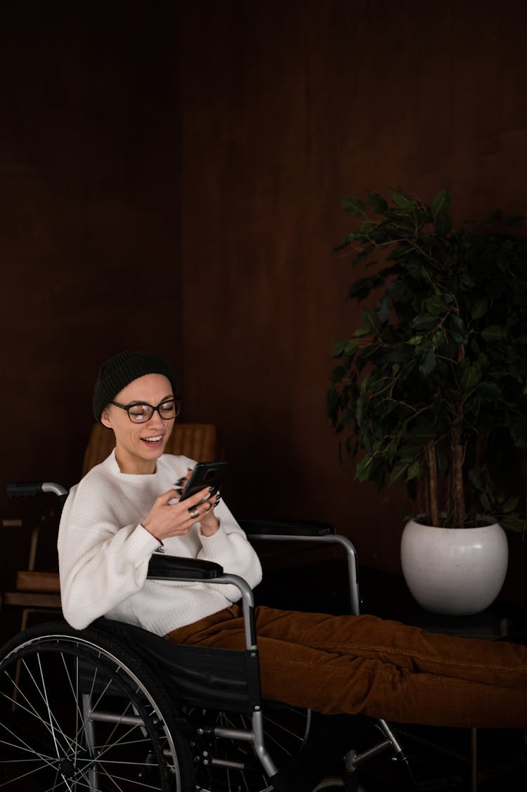 Happy Young Woman Sitting In Wheelchair And Using Smartphone