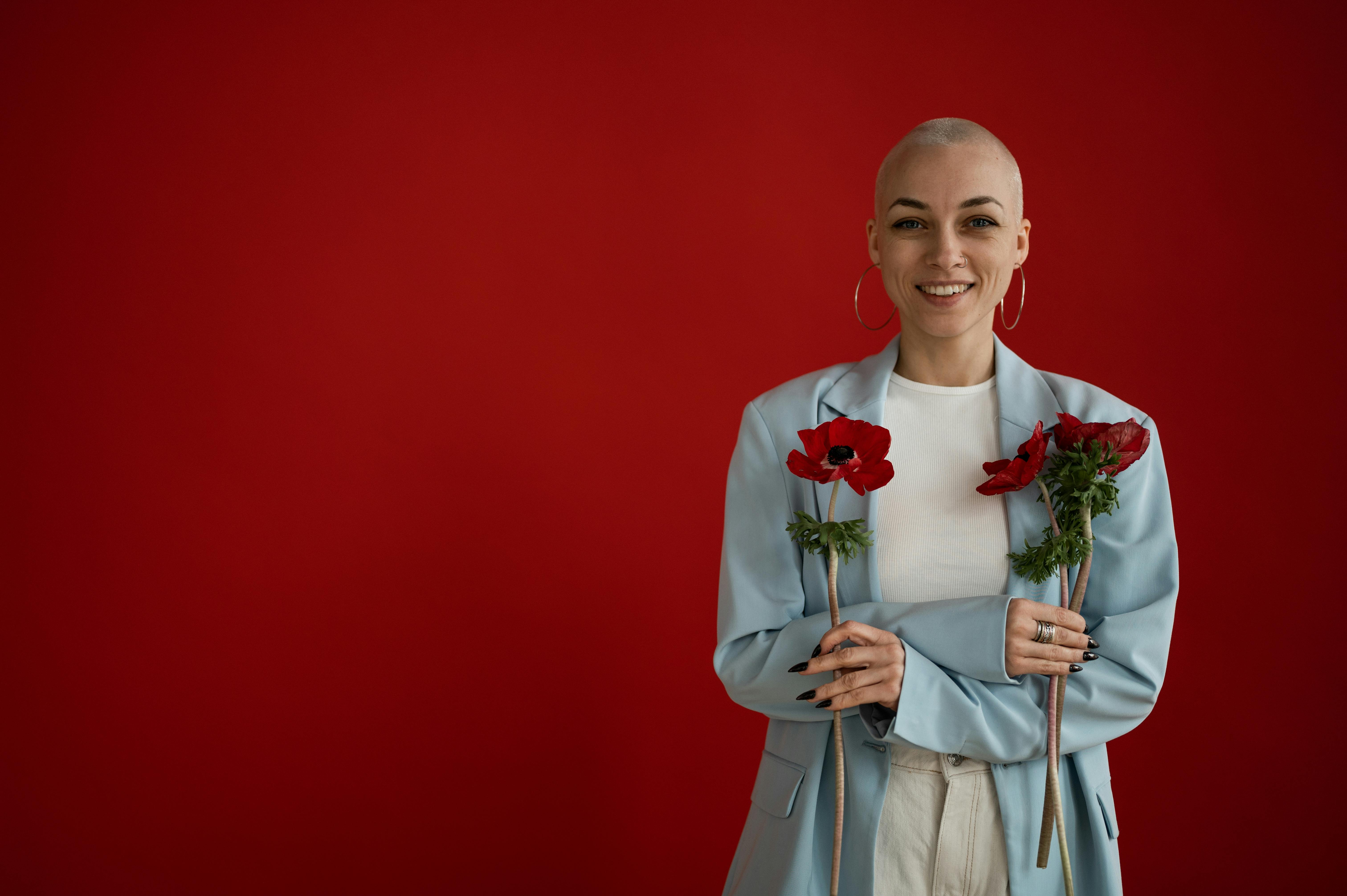 [ColoSach]-a-smiling-young-woman-in-a-blue-jacket-holding-red-flowers,-standing-against-a-vivid-red-background.