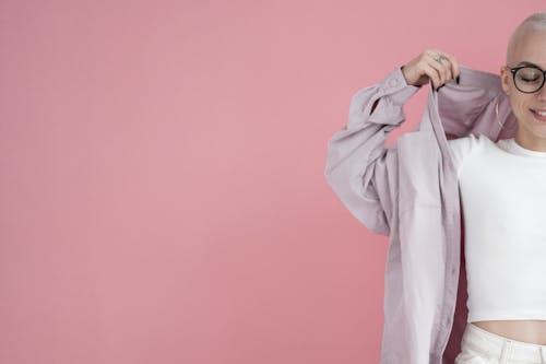 Free Crop cheerful woman with short blond hair standing with closed eyes and adjusting shirt in studio against pink background Stock Photo