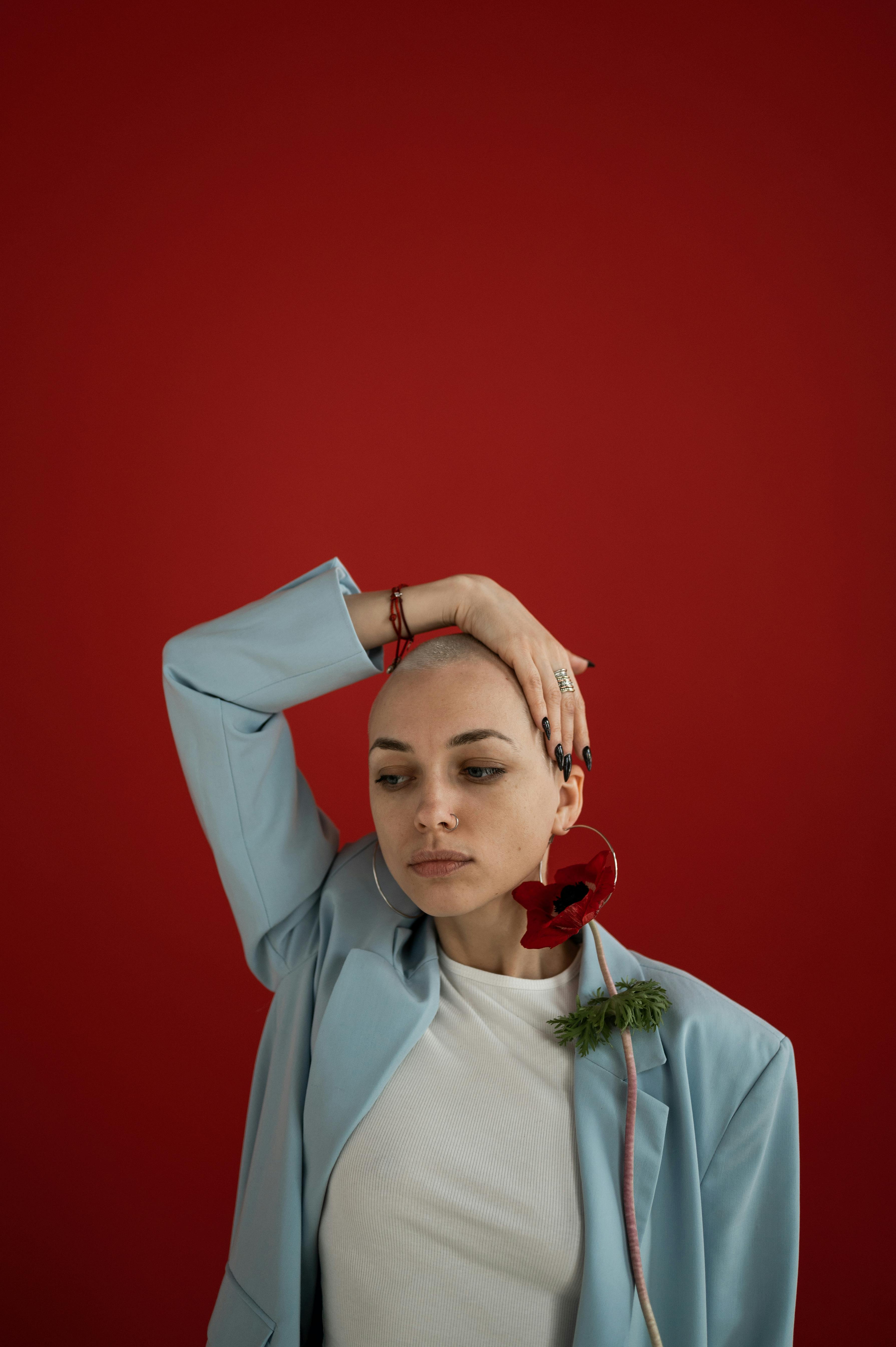 [ColoSach]-serious-female-with-short-hair-and-flower-in-earring-wearing-trendy-outfit-and-touching-head-while-standing-on-red-background-in-studio