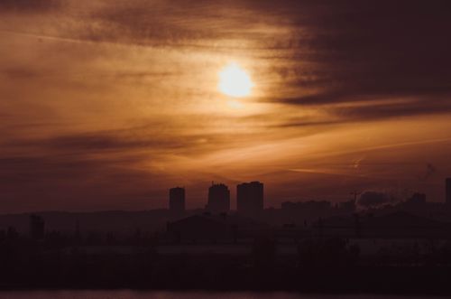 Free Dramatic sunset casting a golden glow over a city skyline in silhouette, offering a serene cityscape view. Stock Photo