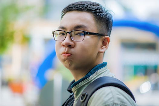 Young man with glasses puffing cheeks outdoors in daylight.