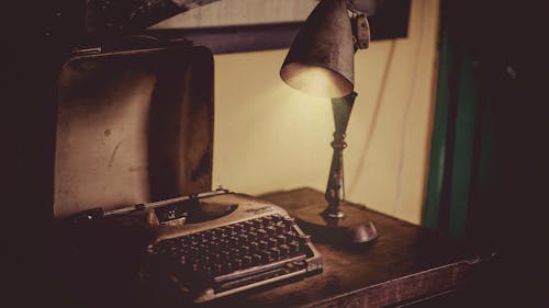 La Fotografía De Sephia De La Lámpara De Escritorio Iluminó La Máquina De Escribir Gris Sobre Una Mesa De Madera