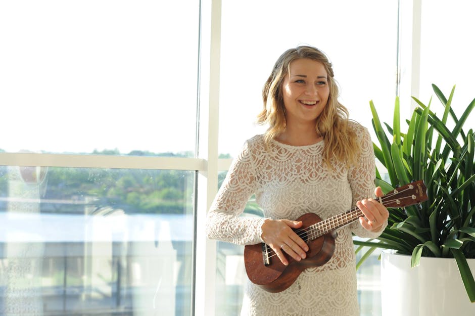 A joyful woman in a lace dress plays a ukulele by a large window. A joyful woman in a lace dress plays a ukulele by a large window.
