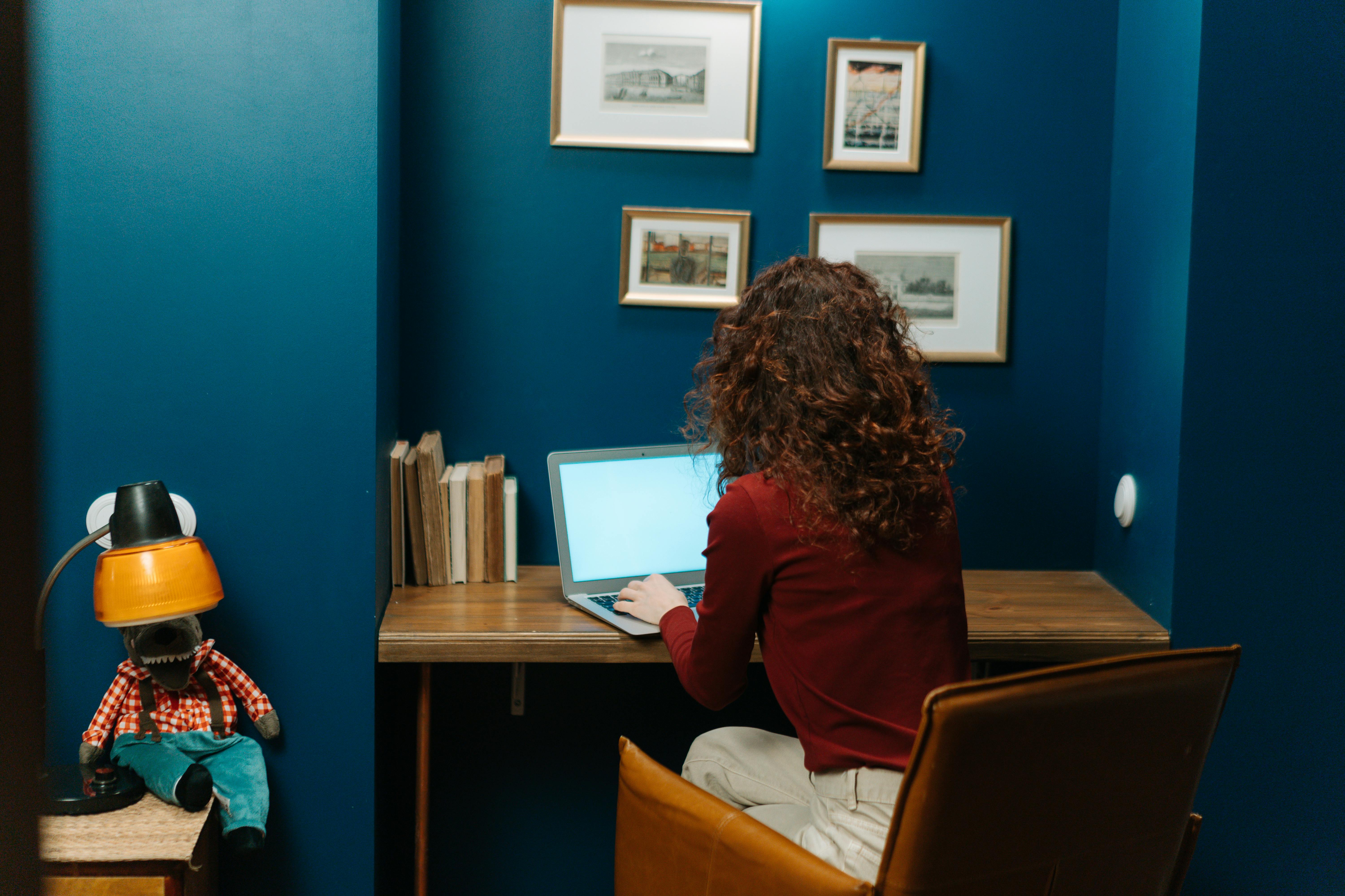Woman with curly hair using a laptop in a modern, cozy home office with vibrant decor.