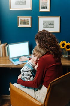 A mother works on a laptop with her child sitting on her lap, showcasing work-life balance.