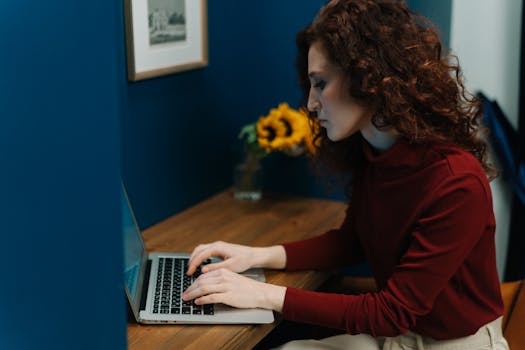 A woman working on a laptop at a desk with sunflowers, surrounded by blue decor, focusing intently.