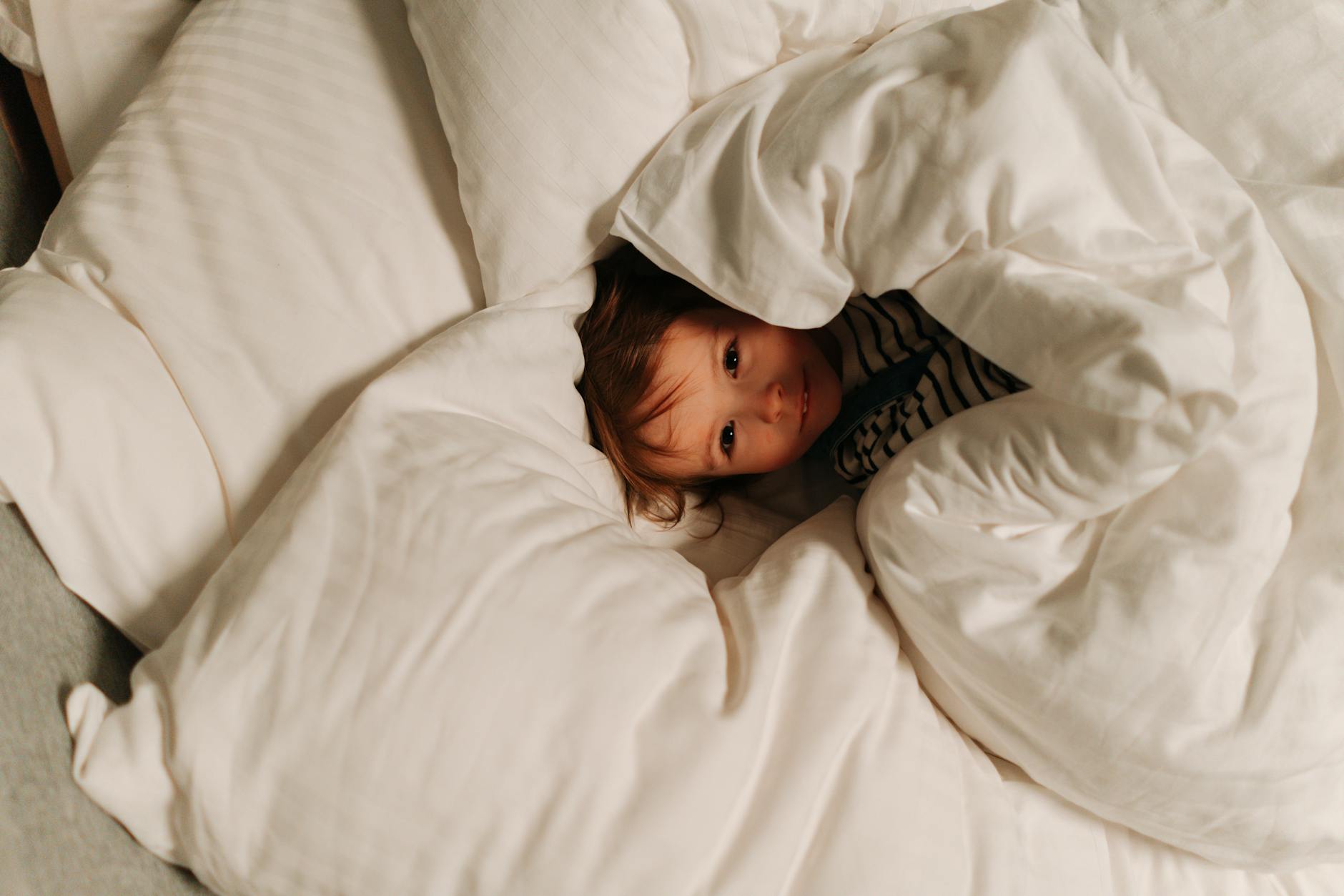 Child laying in bed covered with blanket