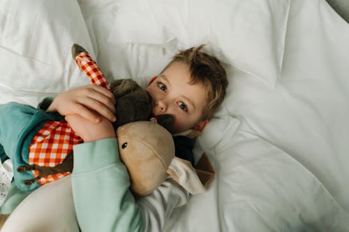 Free A Kid Lying On Bed Hugging His Stuffed Toys Stock Photo