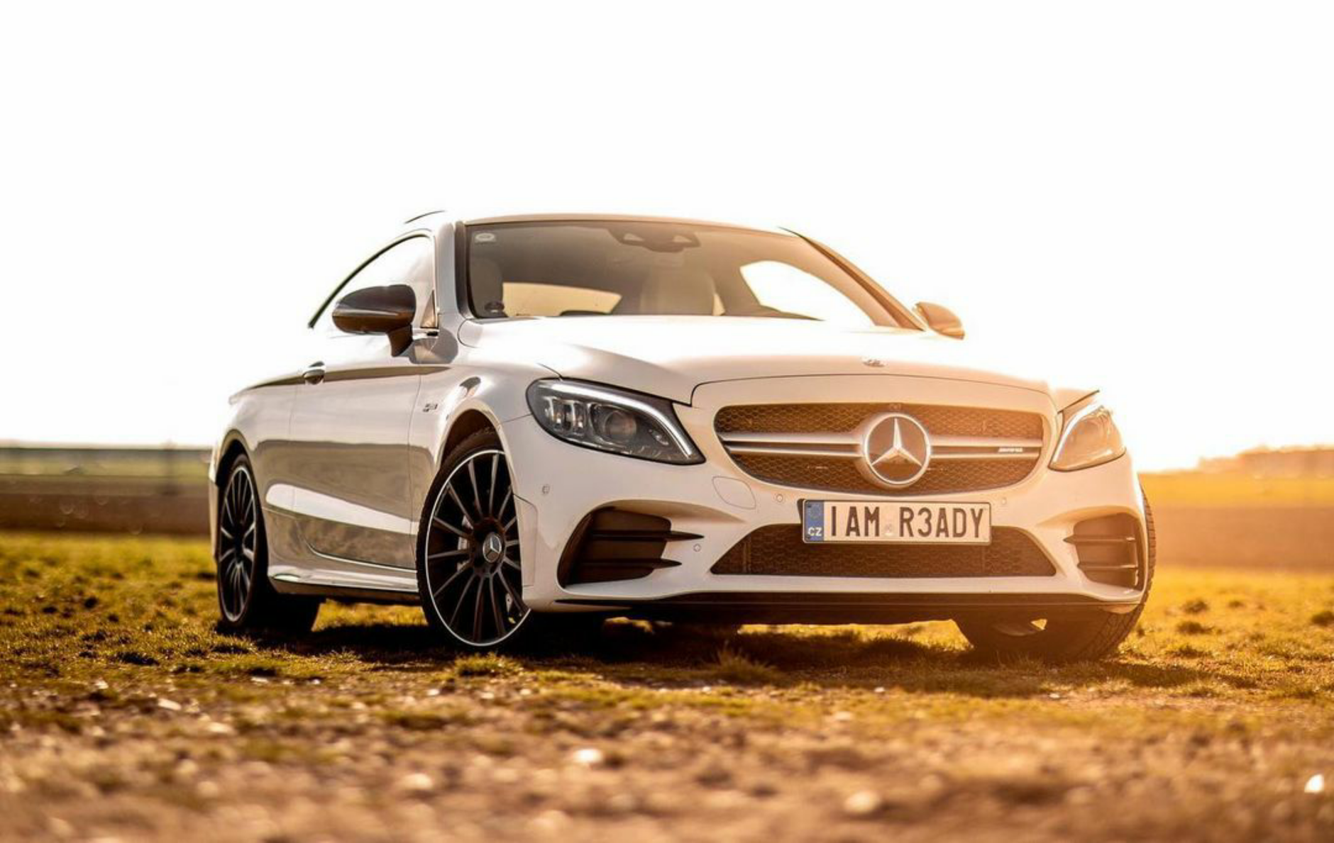 A sleek white Mercedes Benz parked in a sunlit field, showcasing luxury and elegance.