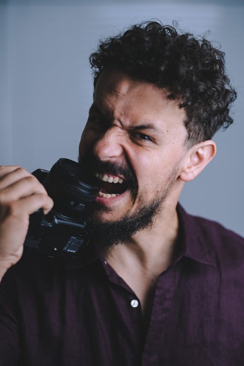 Foto profissional grátis de cara comendo uma camera, cara de bravo, cara mordendo uma câmera