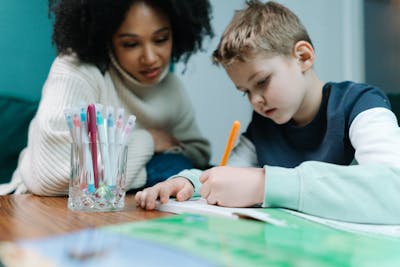 A young student writing attentively while a teacher provides supportive, patient guidance