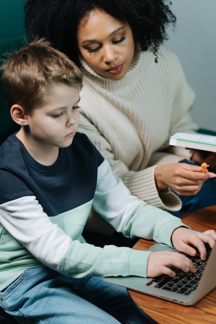 A Woman Tutoring A Boy Typing On A Laptop