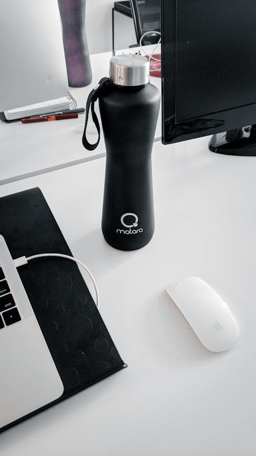 Free High angle of water bottle on white desk near netbook and mouse near computer monitor placed in bright office Stock Photo