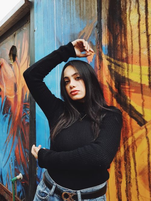Free Confident woman posing against a vibrant wall mural outdoors. Stock Photo