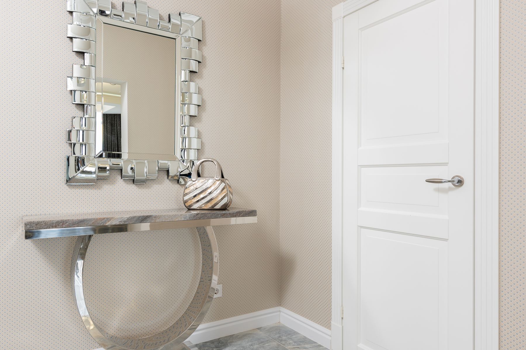 Slim metallic console beside an entrance door with a handbag resting beneath a wall mirror
