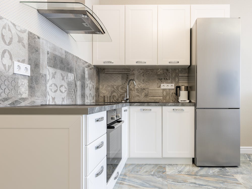 Free Modern kitchen interior with white cabinets and fridge against electric kettle and ornamental wall in light house Stock Photo