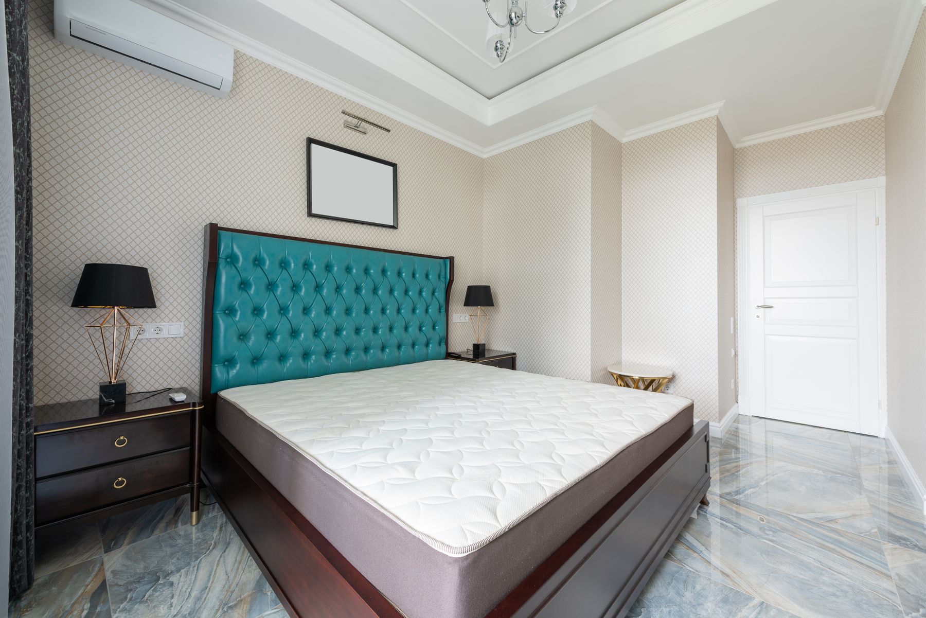 Spacious bedroom with a broad teal upholstered bed, paired nightstands, warm lamps and pale floor