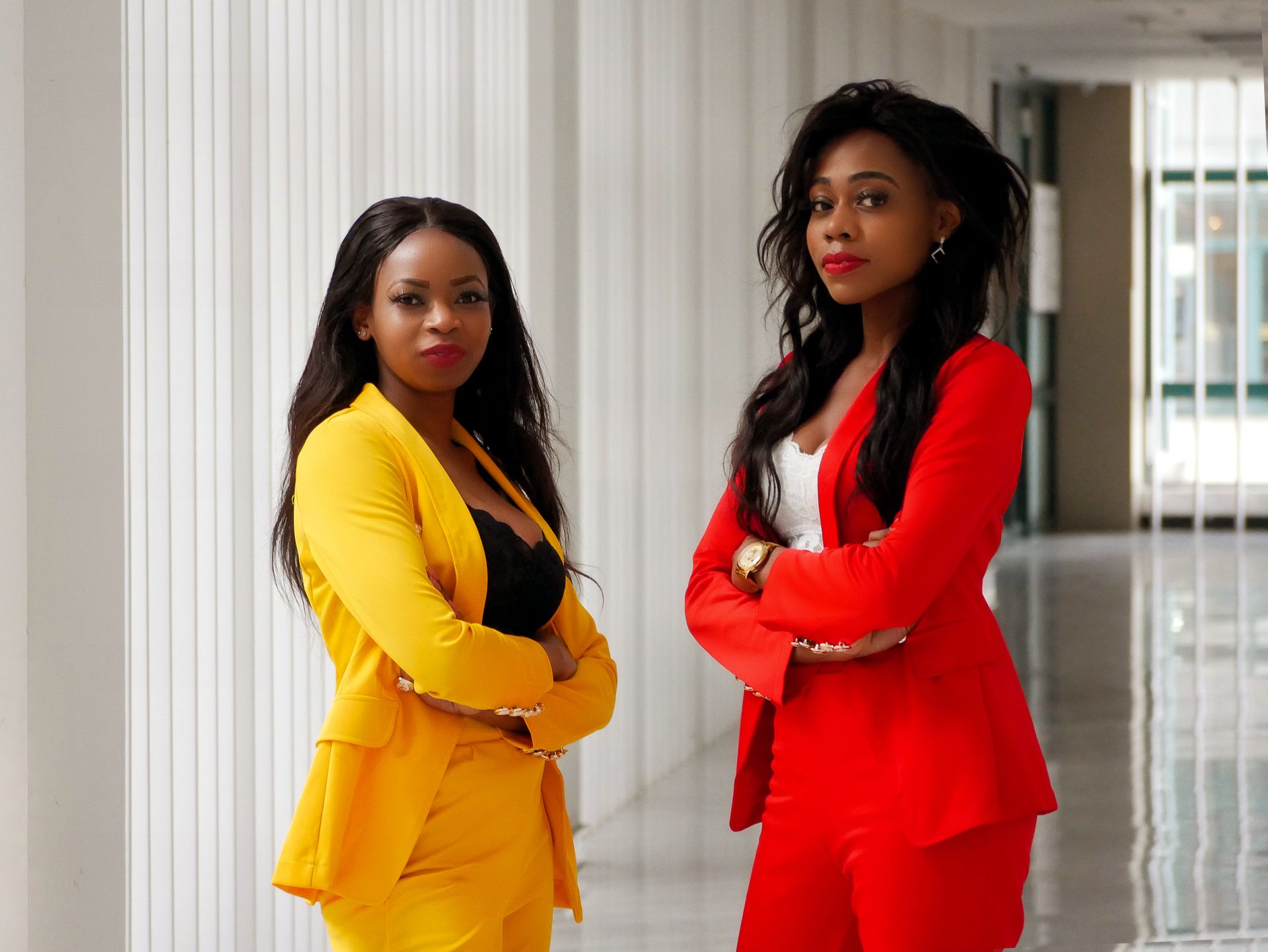 Two confident women in vibrant business suits posing indoors, showcasing empowerment and style.