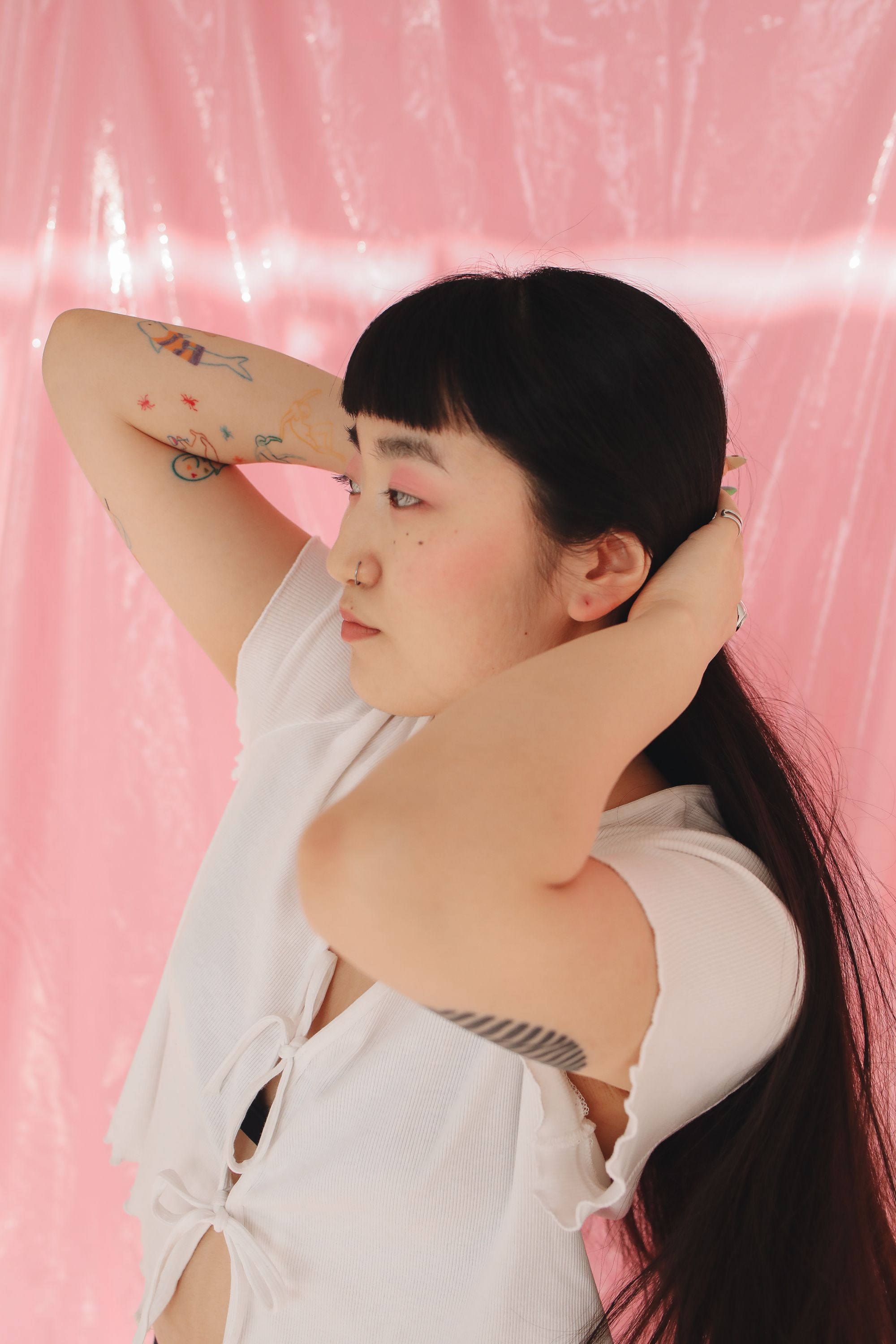 Woman with tattoos adjusting her hair in front of a pink backdrop. Captivating lifestyle portrait.