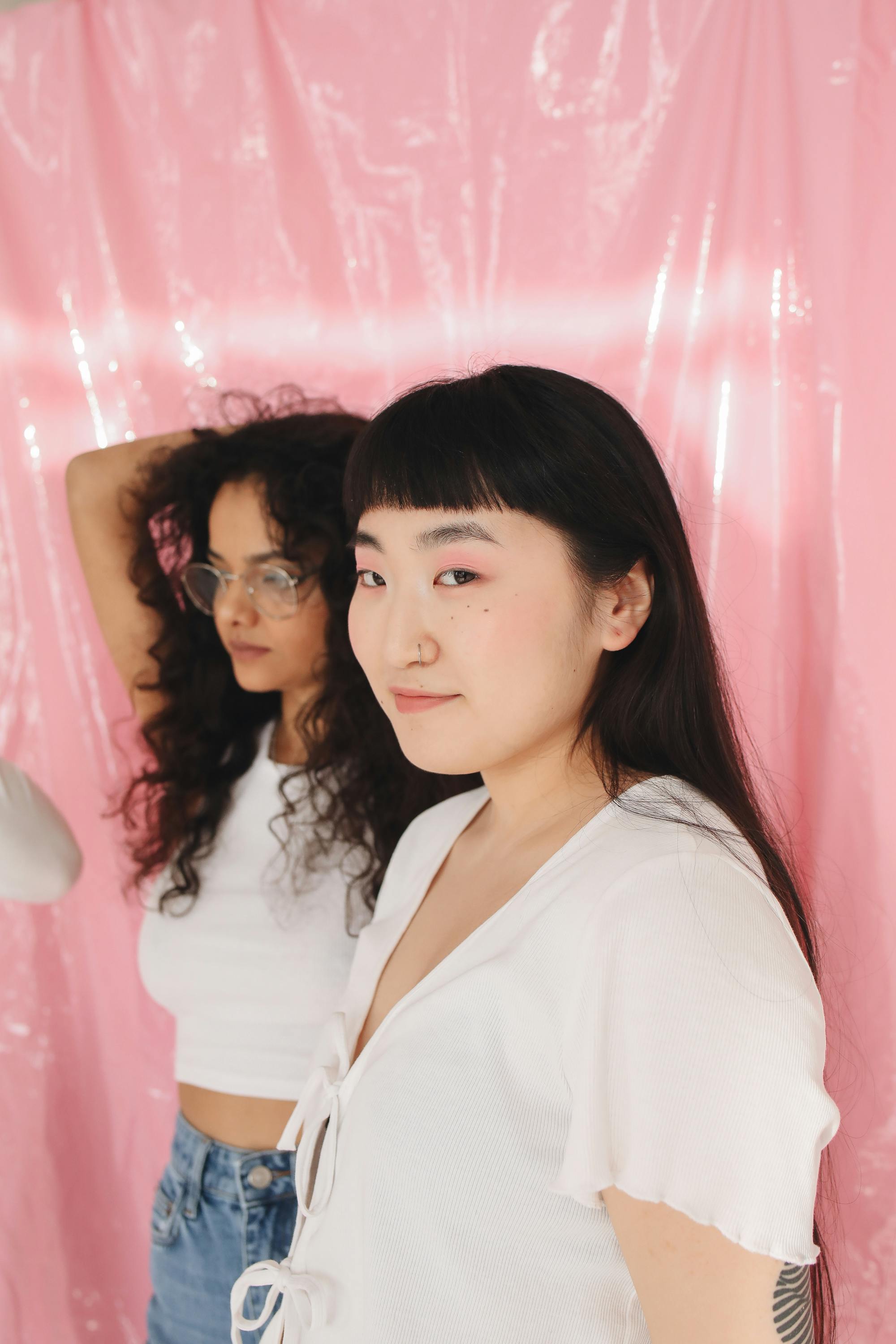 Two young women with diverse looks posing stylishly against a pink backdrop.