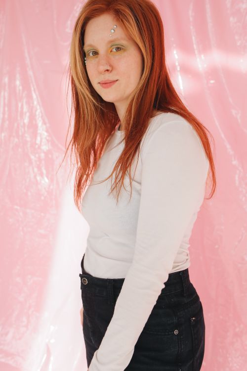 Free A young caucasian woman poses with a soft smile, set against a pink backdrop. Stock Photo