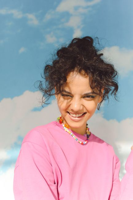 Bright portrait of a smiling woman wearing a pink shirt against a clear sky backdrop.