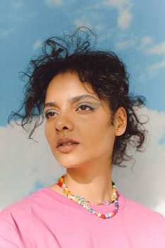 A vibrant portrait of a woman in a pink shirt with artistic makeup against a sky backdrop.