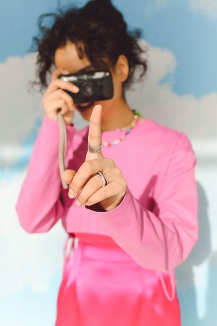 Teen capturing a moment with camera, wearing a stylish pink dress and rings.