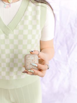 Fashionable person holding a glittery Airpods case with stylish nails and checkered outfit.