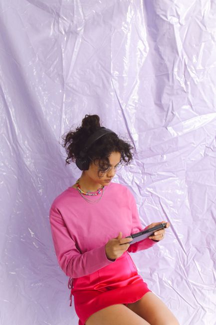 A stylish woman in pink using a tablet, wearing headphones against a textured background.