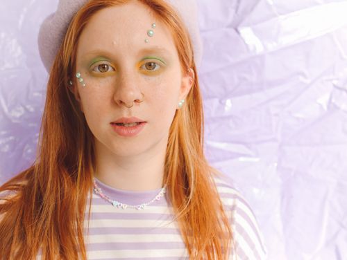 Free Young woman wearing a beret with artistic makeup and jewelry, set against a pastel background. Stock Photo
