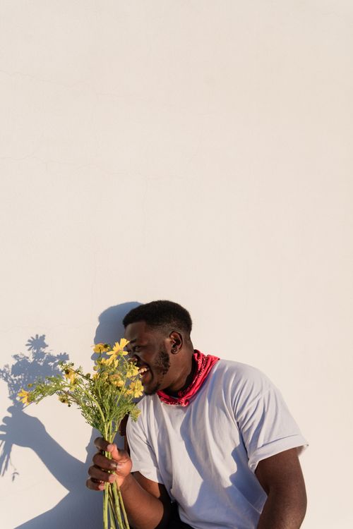 Free Cheerful man with yellow flowers enjoys the sunlight against a white background. Stock Photo