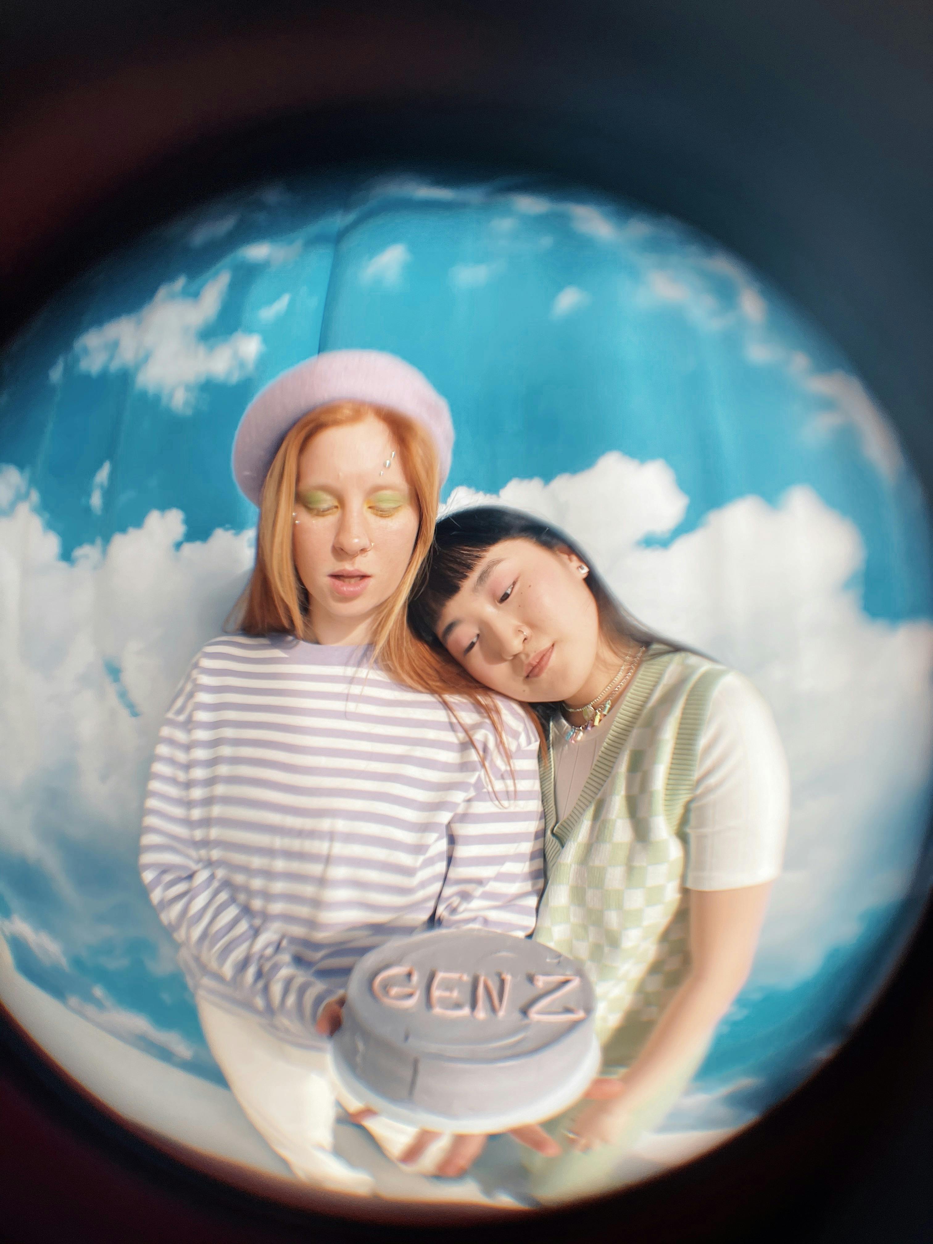 Two Gen Z friends holding a cake under a fisheye lens, showcasing modern friendship and celebration.