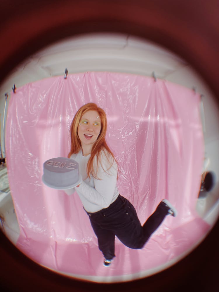 Fisheye Photo Of A Woman With Red Hair Holding A Gen Z Cake