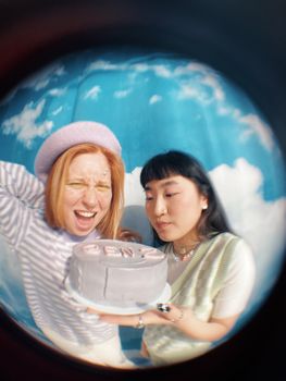 Two cheerful girls celebrating with a trendy Gen Z cake captured in a fisheye view.