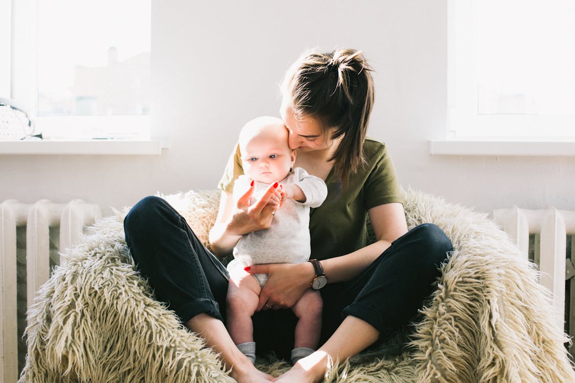 Woman Holding Baby While Sitting on Fur Bean Bag