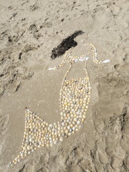 Artistic mermaid design crafted with shells on a sunny sandy beach, perfect for summer and travel themes.