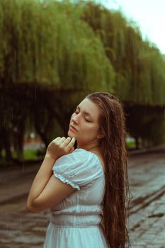 A woman poses gracefully in the rain, feeling serene in an outdoor setting with lush greenery.