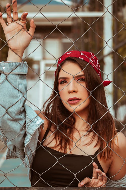 Woman in a Red Bandana Posing Near a Chain Link Fence