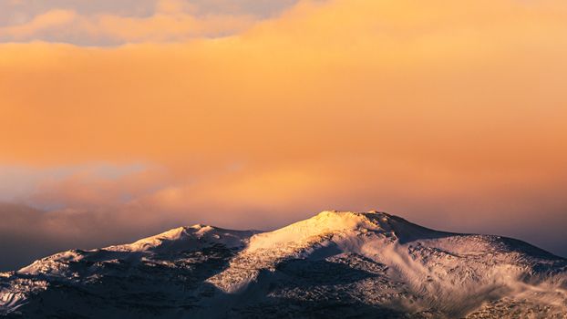 Breathtaking view of snow-covered Norway mountains under a dramatic sunset sky.