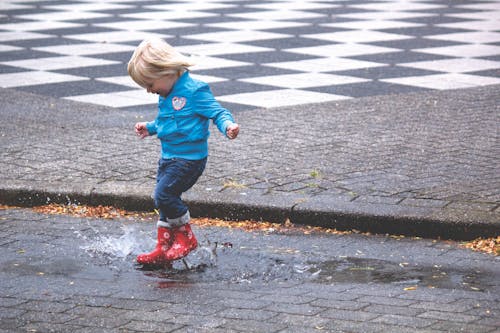 Boy in Blue Jacket Hopping on Water Puddle