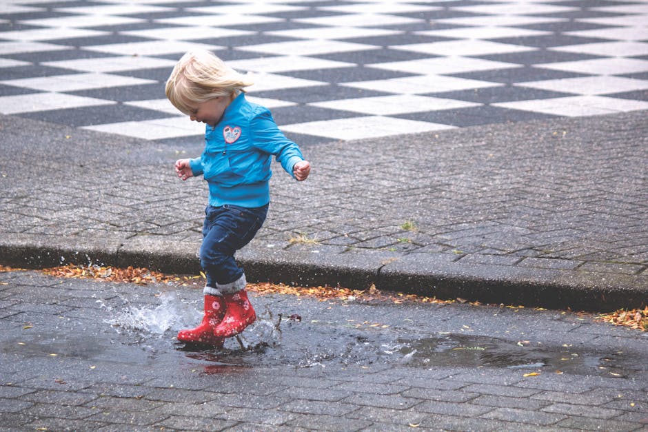 Boy in Blue Jacket Hopping on Water Puddle